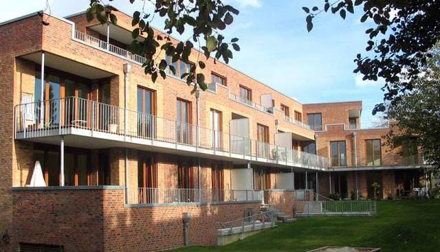 Modernes Backstein-Mehrfamilienhaus mit Balkonen und einem begrünten Innenhof unter Bäumen