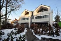 Schneebedecktes, modernes zweistöckiges Haus mit weißen Balkonen und kahlen Bäumen davor