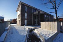 Modernes Backstein-Mehrfamilienhaus neben einem schneebedeckten Gehweg und Zaun an einem sonnigen Tag