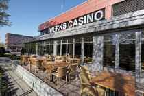 Sitzgelegenheiten im Freien vor einem WERKS CASINO-Gebäude mit Glasfassade