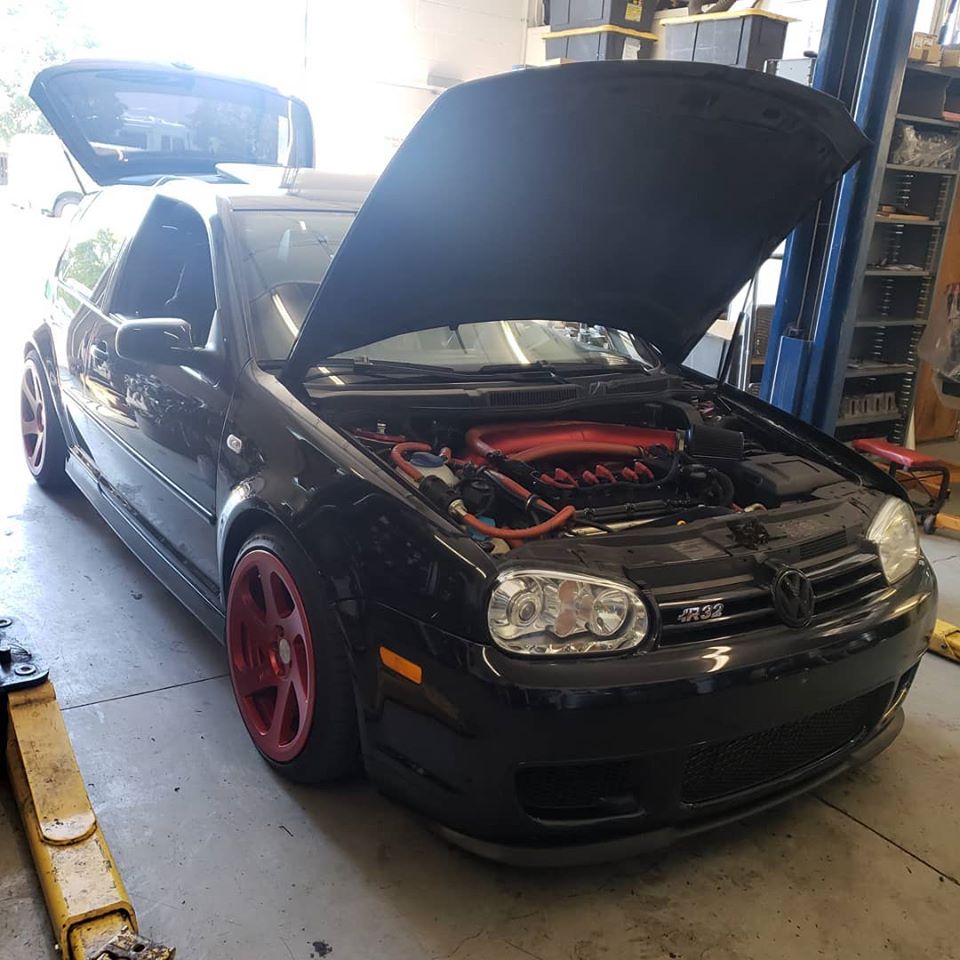 A black volkswagen R32 Golf with the hood open is parked in a garage.