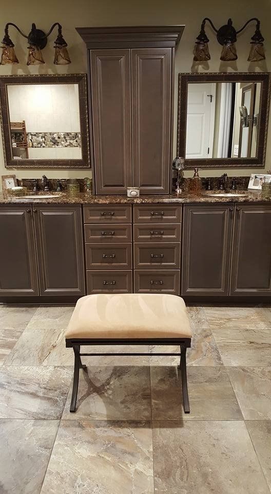 Bathroom with a vanity, cabinets, and a stool. Gray cabinets, tan floor, and light fixtures.