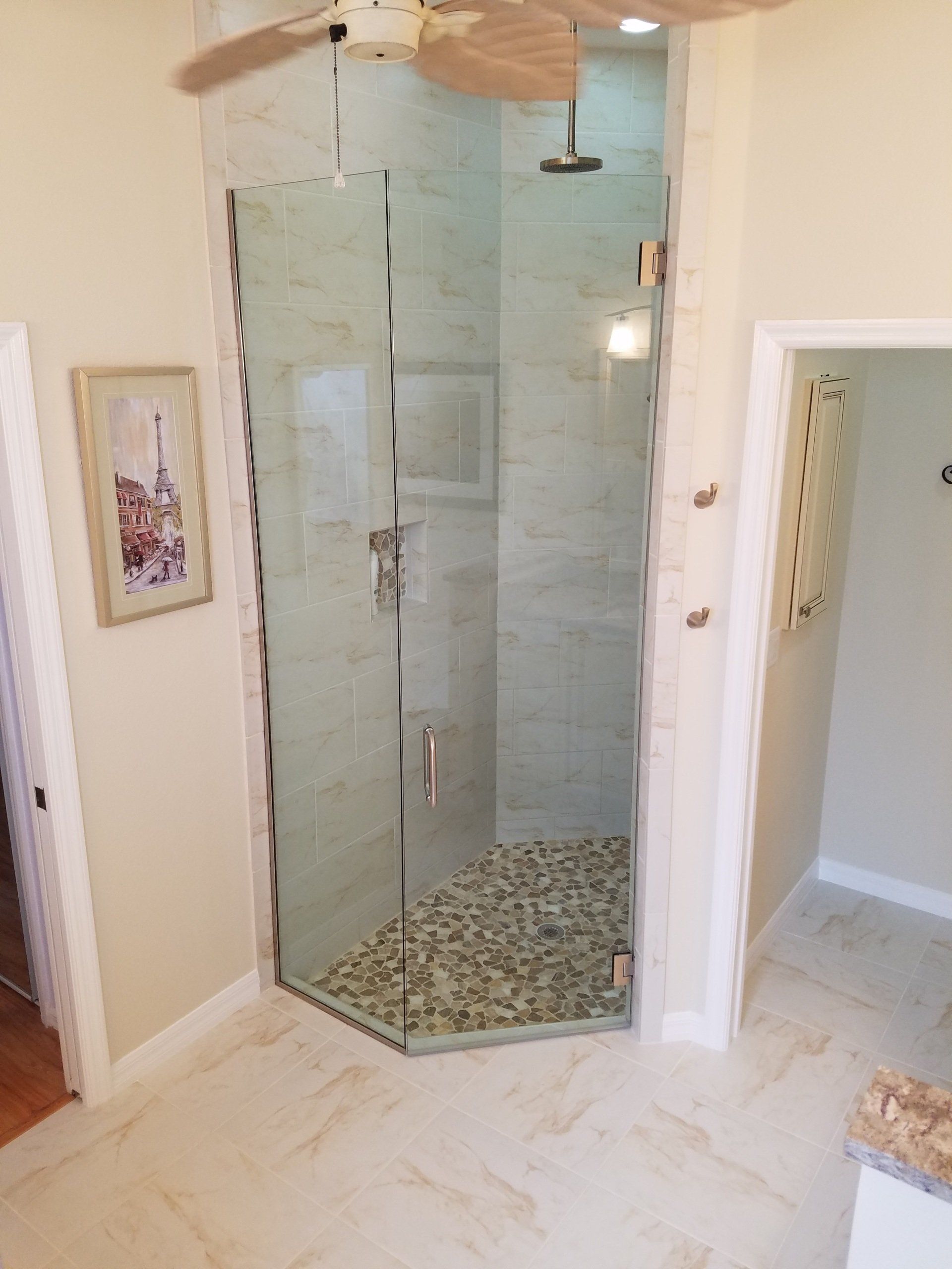 A corner shower with glass doors. Beige tile floor and walls. Pebbled shower base.