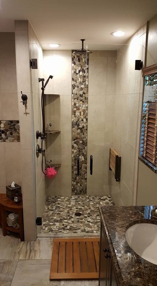 Shower with stone floor and accent strip, glass door, neutral tile, and dark fixtures.