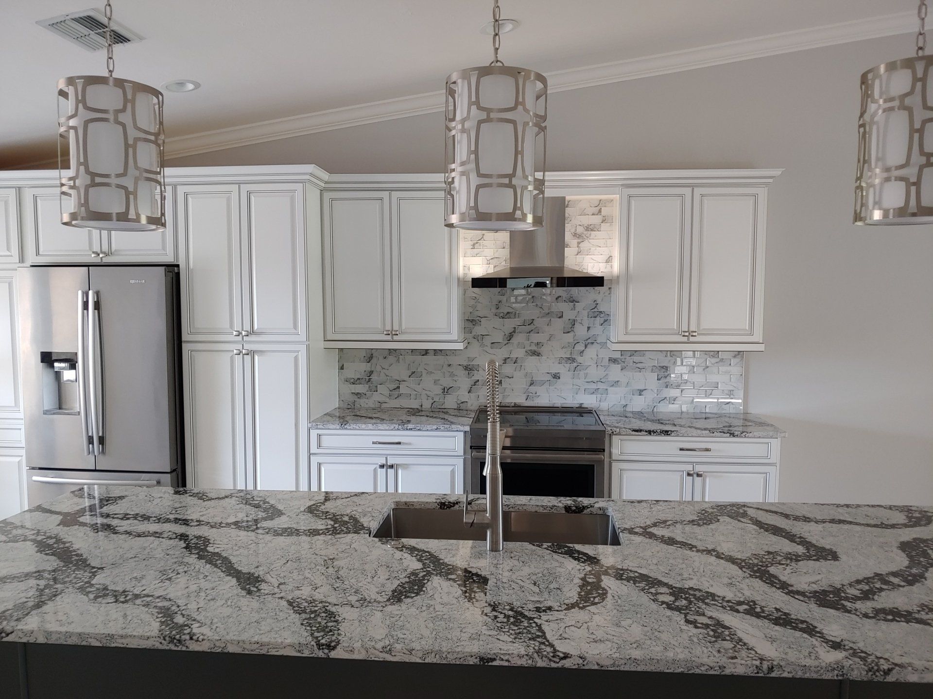 White kitchen with granite countertop, stainless steel appliances, and pendant lights.