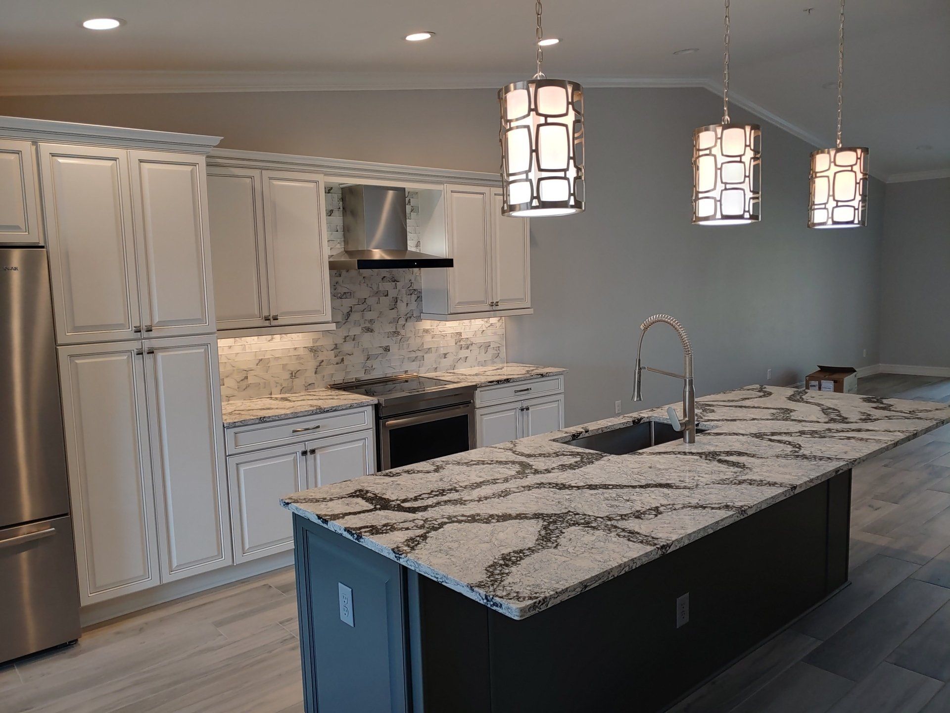 Modern kitchen with white cabinets, granite countertops, and three hanging lights.