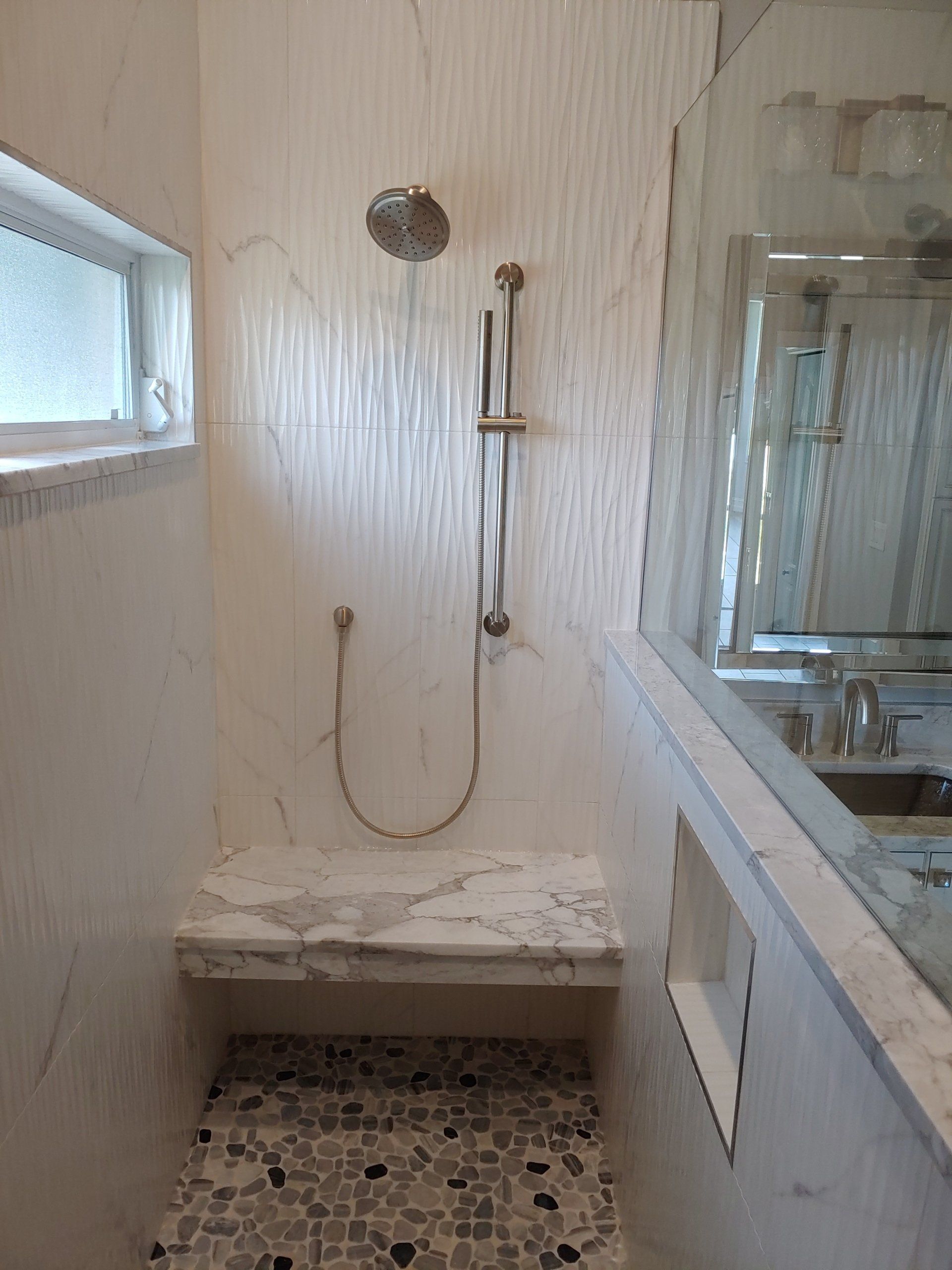 A modern bathroom shower with a marble bench and pebble floor.