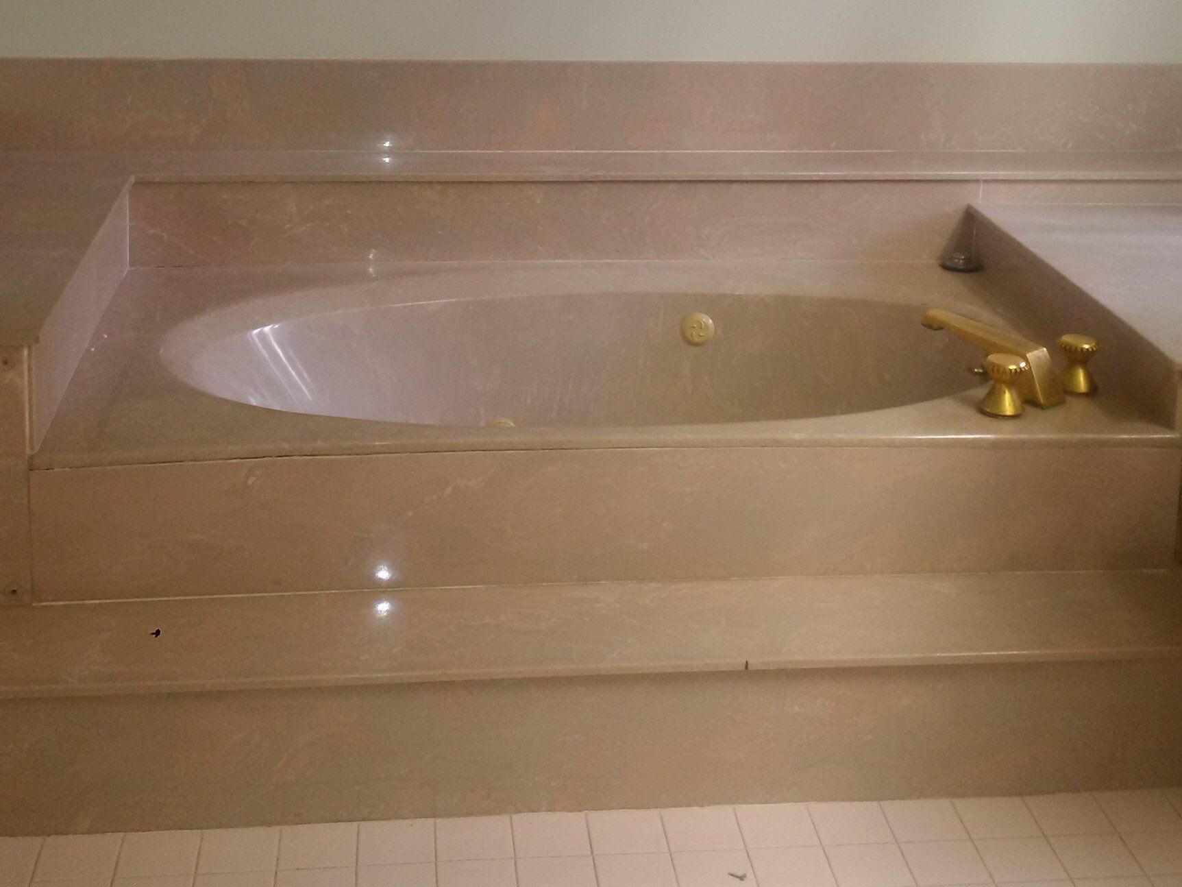 Oval jacuzzi tub with gold fixtures surrounded by beige stone steps.