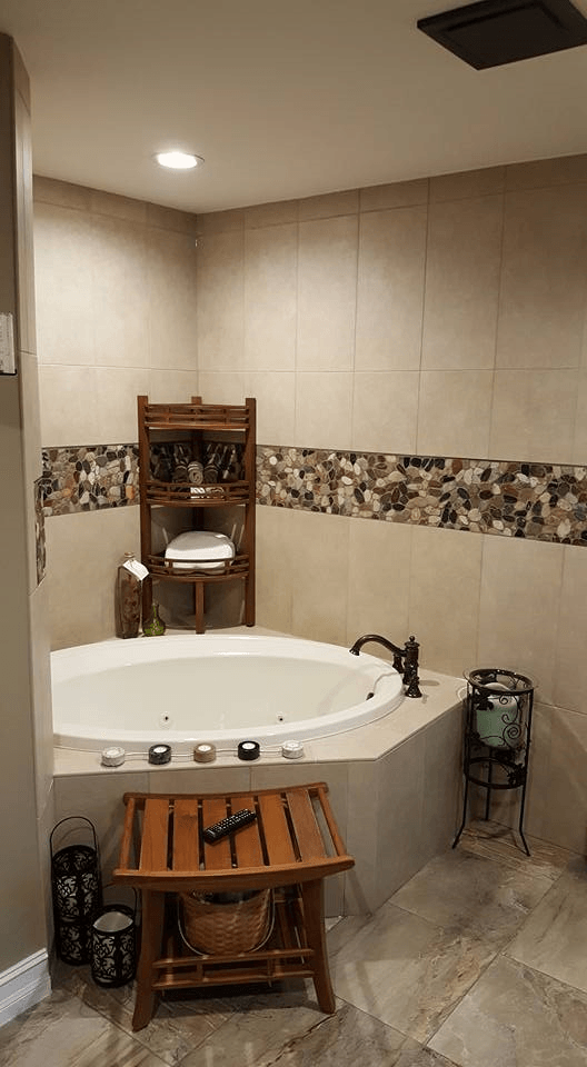 Cozy bathroom with corner jacuzzi tub, stone tiles, wooden accents, and candle decorations.