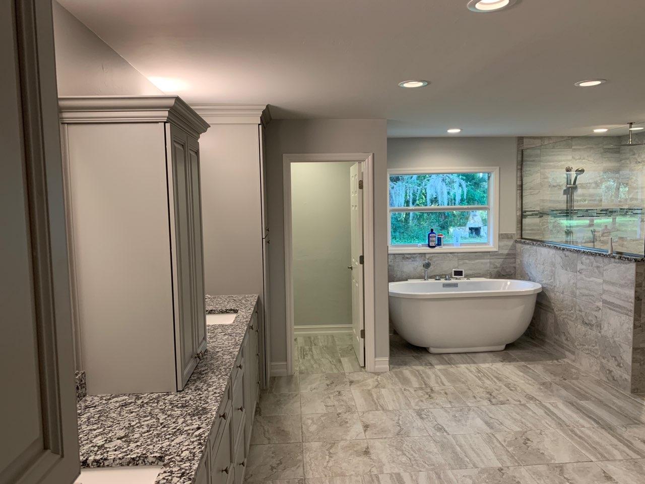 Bathroom with gray cabinets, granite countertops, soaking tub, and a tiled shower.