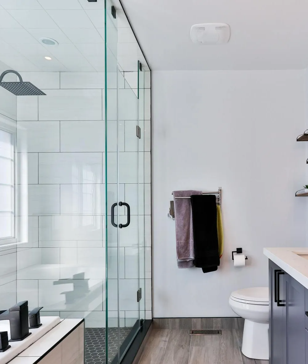 Modern bathroom with glass shower, white walls, toilet, and towels. Gray and light wood color scheme.