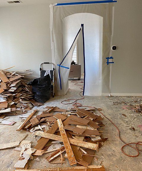 Room with hardwood floor removal debris, doorway sealed with plastic, and a black trash bag.
