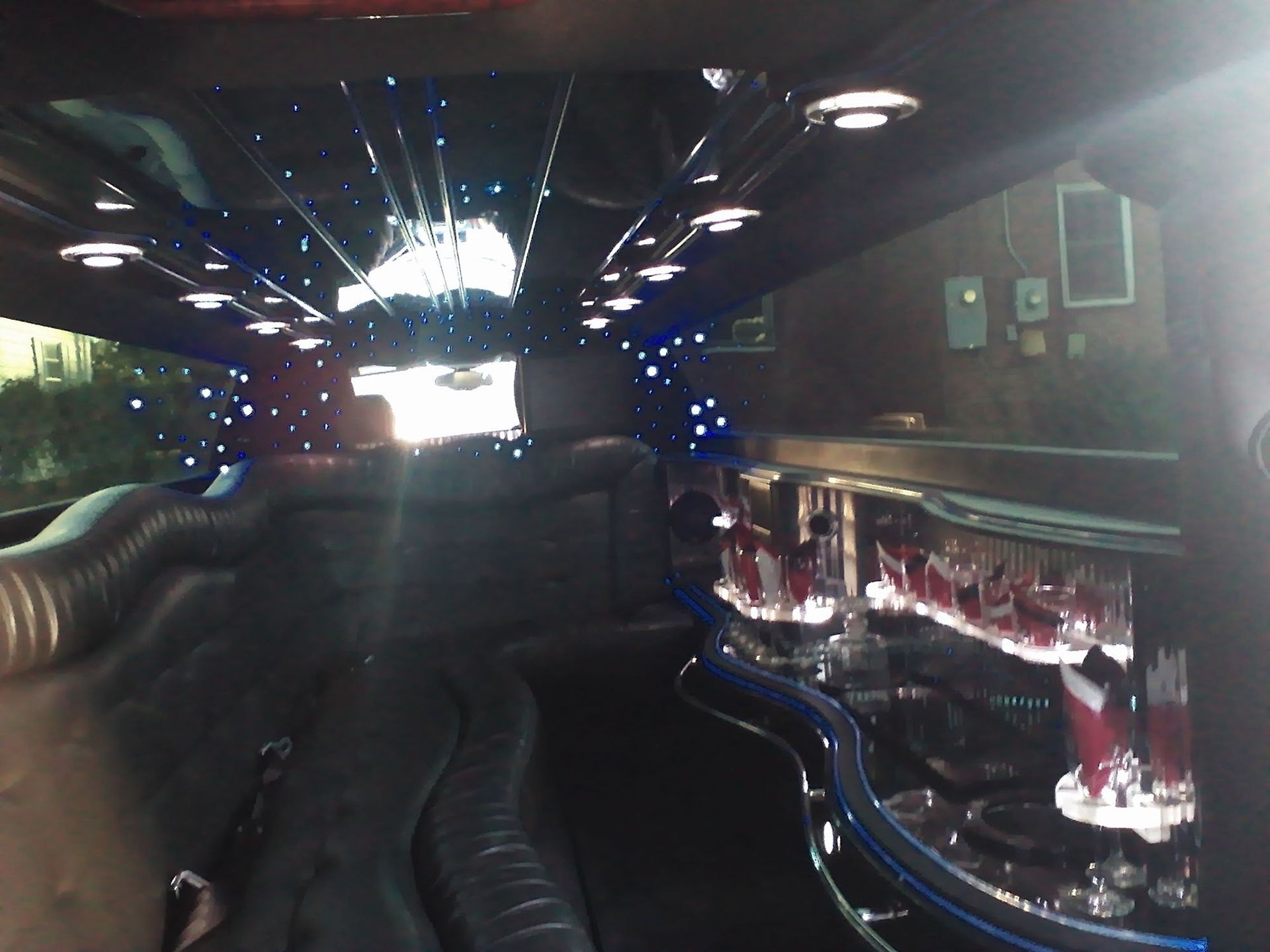 Interior view of a luxurious black limousine with leather seats, fiber optic ceiling lights, and an illuminated bar area.