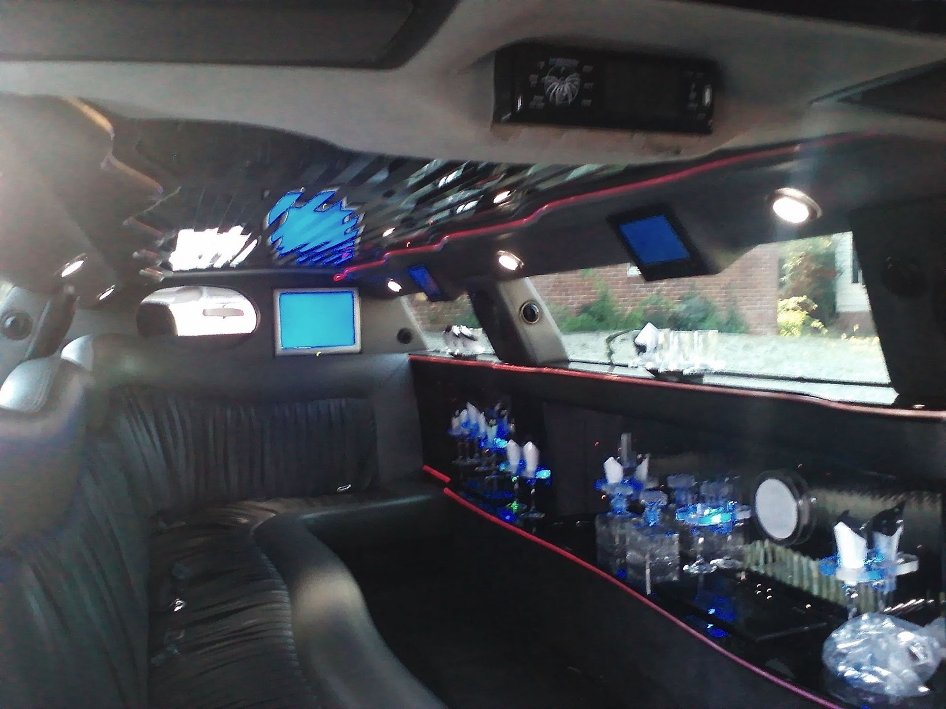 Interior view of a limousine with black leather wrap-around seating, blue accent lighting, and a bar area with glassware.
