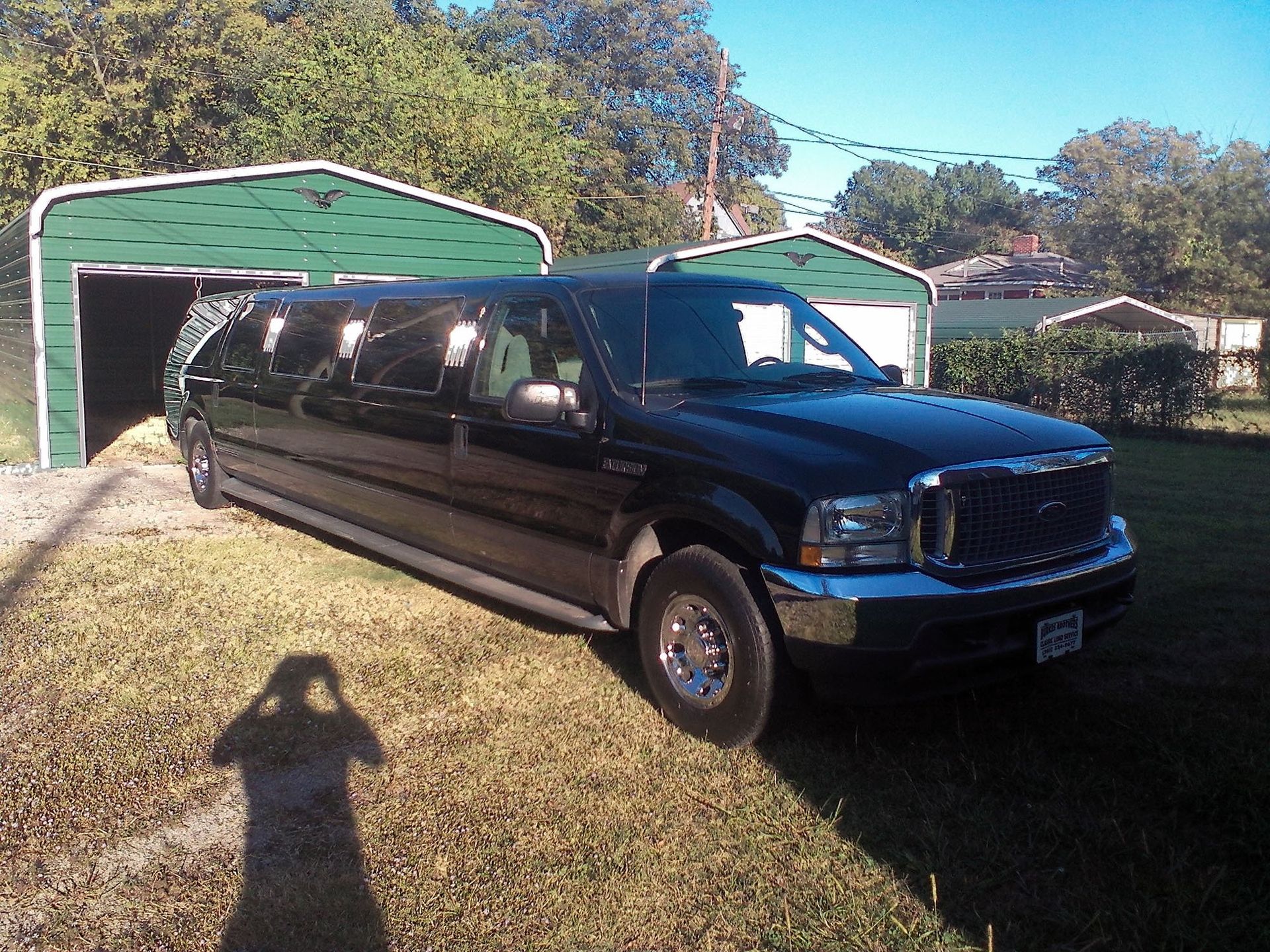 A black stretch limousine parked on a lawn in front of green metal storage sheds.
