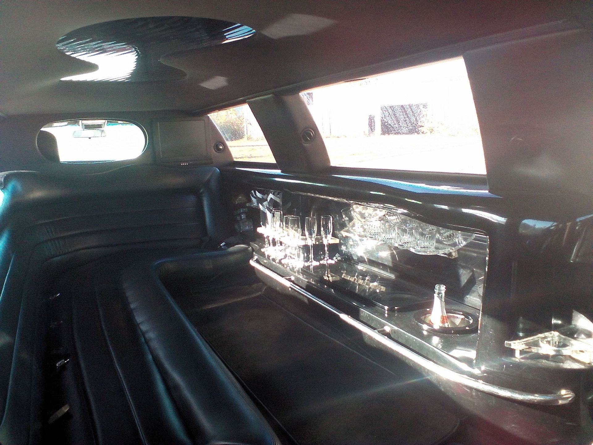 The interior of a black limousine, showing leather seating and a reflective bar area with glassware.