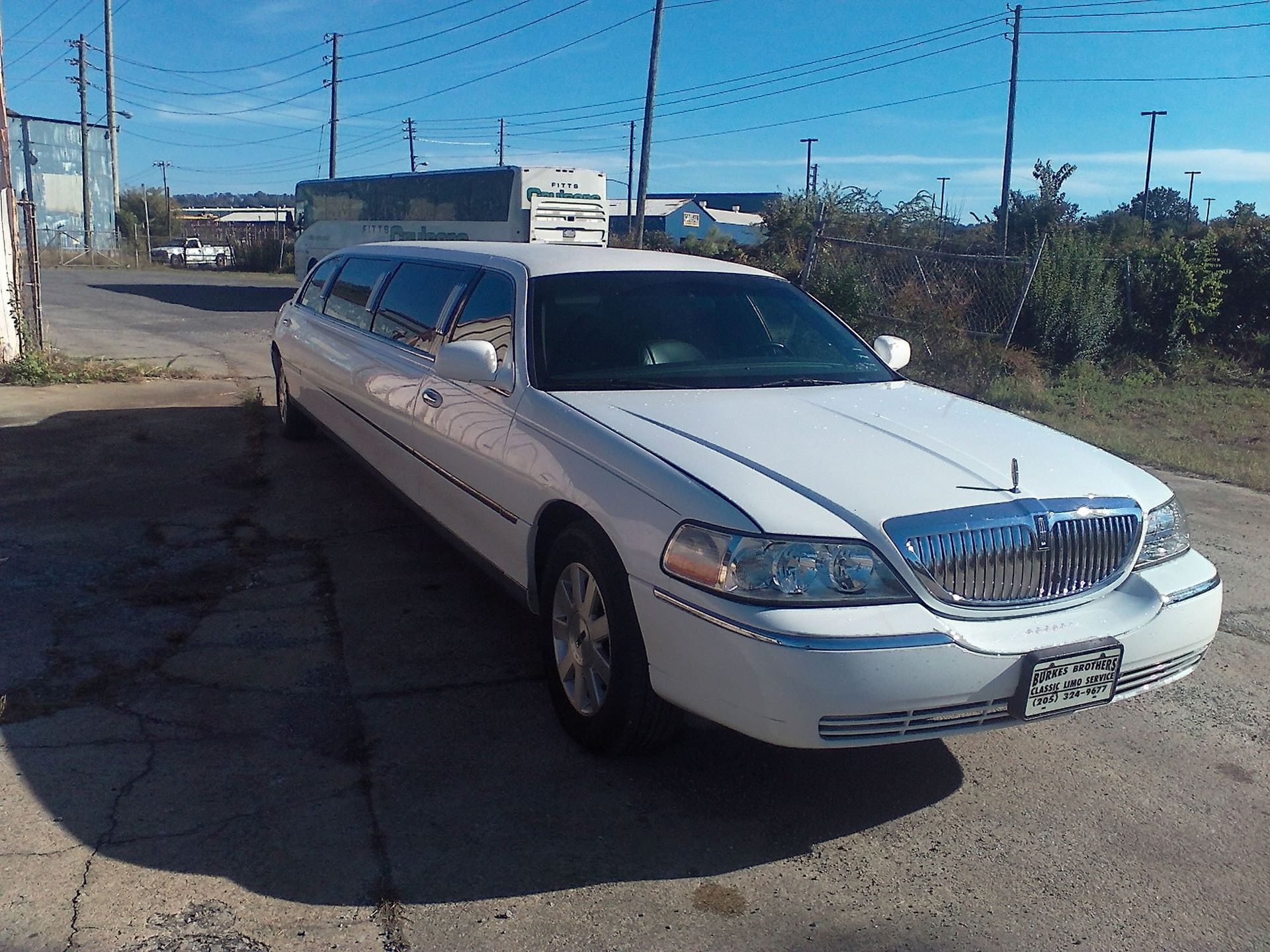 A white Lincoln limousine parked on a paved lot on a sunny day.