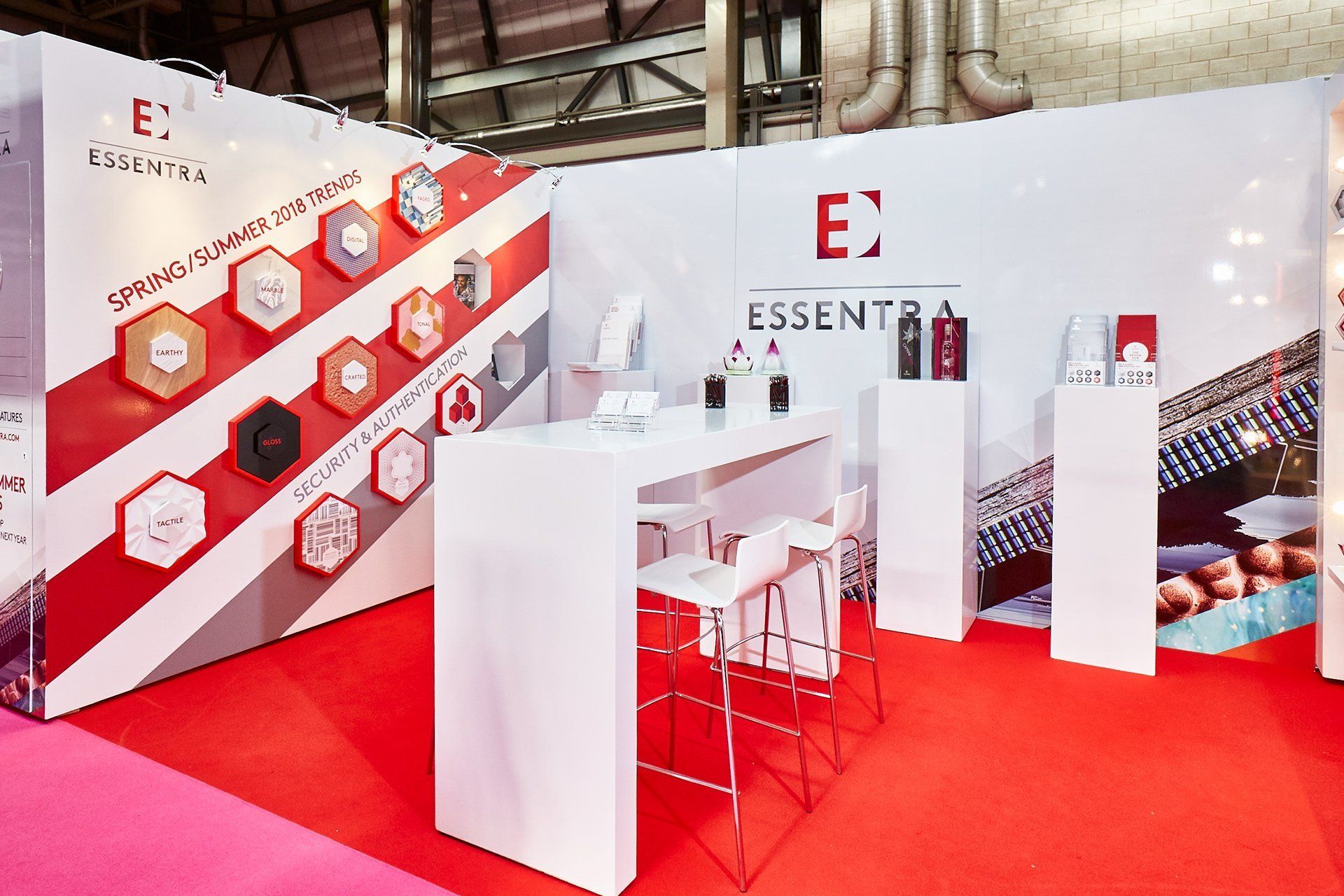 A booth with a red carpet and white tables and stools