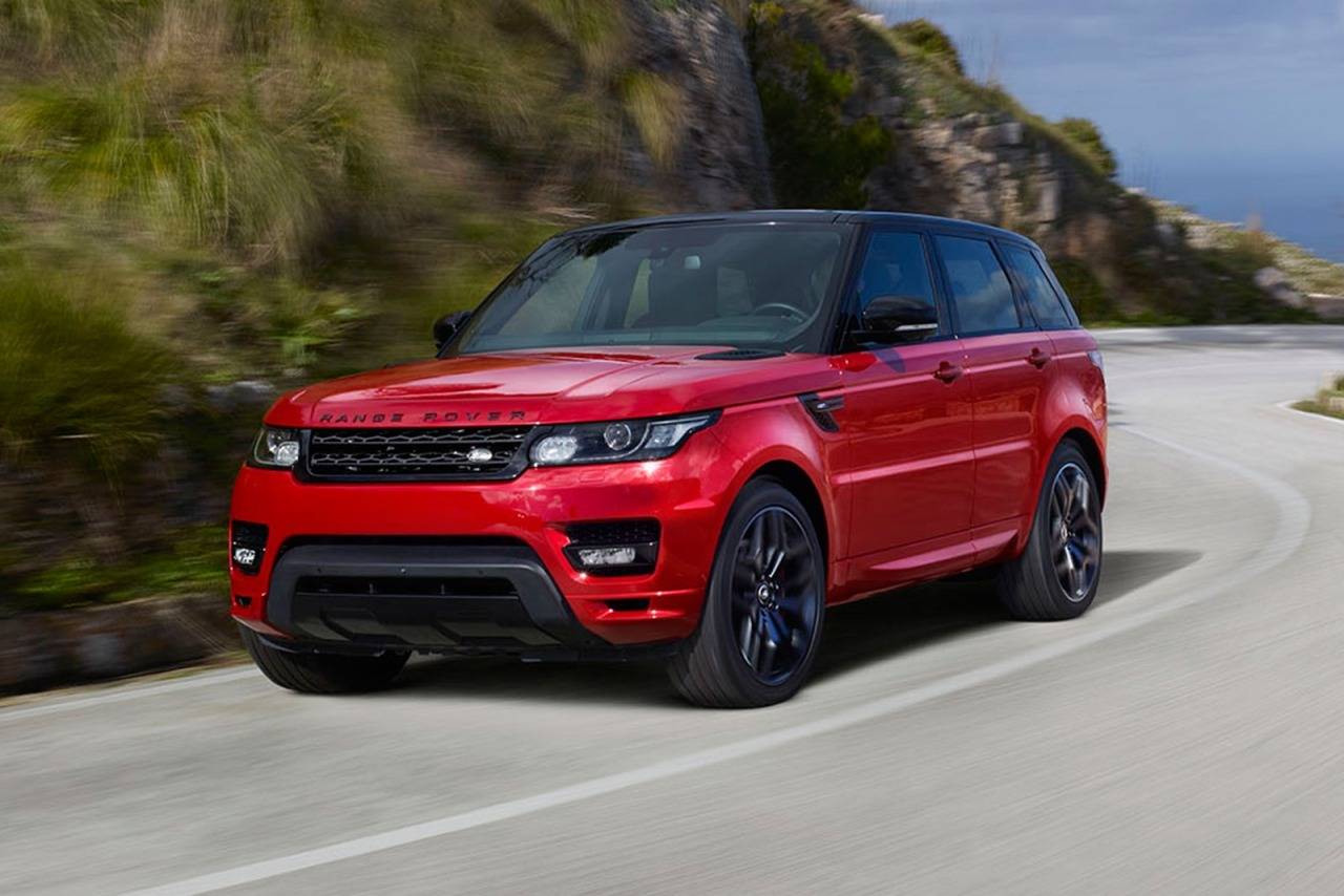 Red Range Rover Sport SUV driving on a winding road with a black roof, near a hillside.