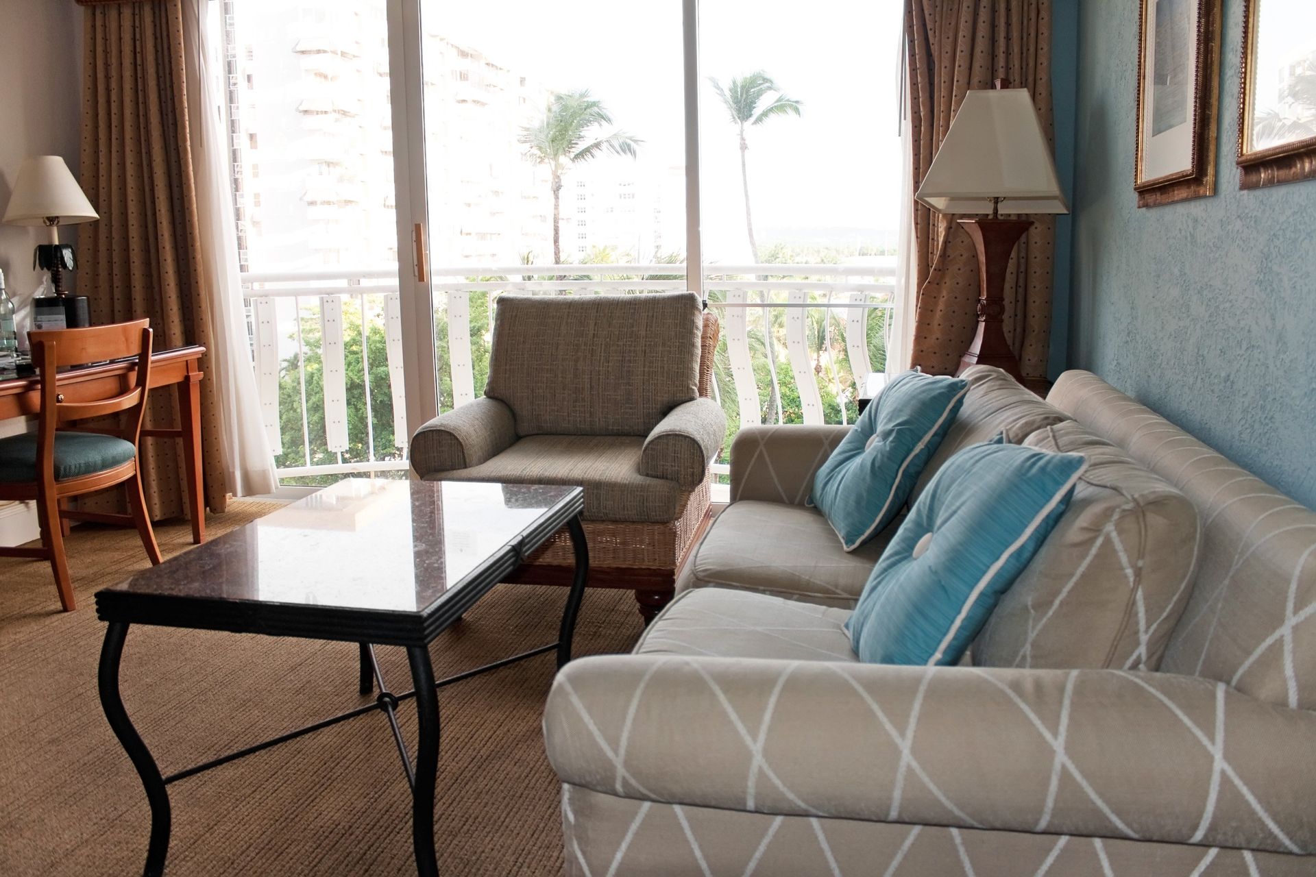 Living room with a couch, armchair, desk, and view from a balcony.