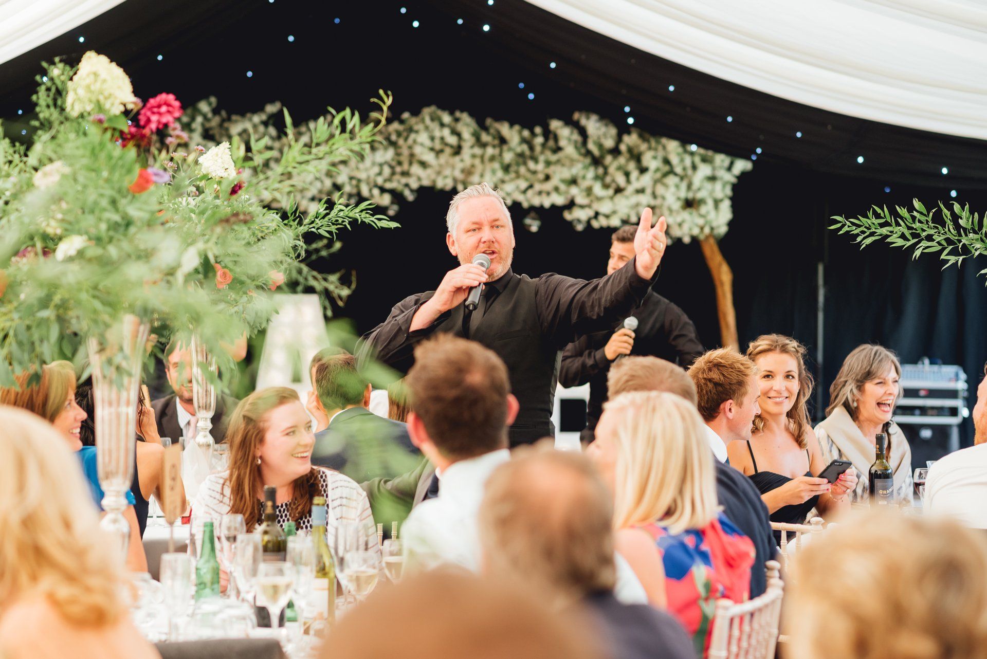 A man is speaking into a microphone at a wedding reception.