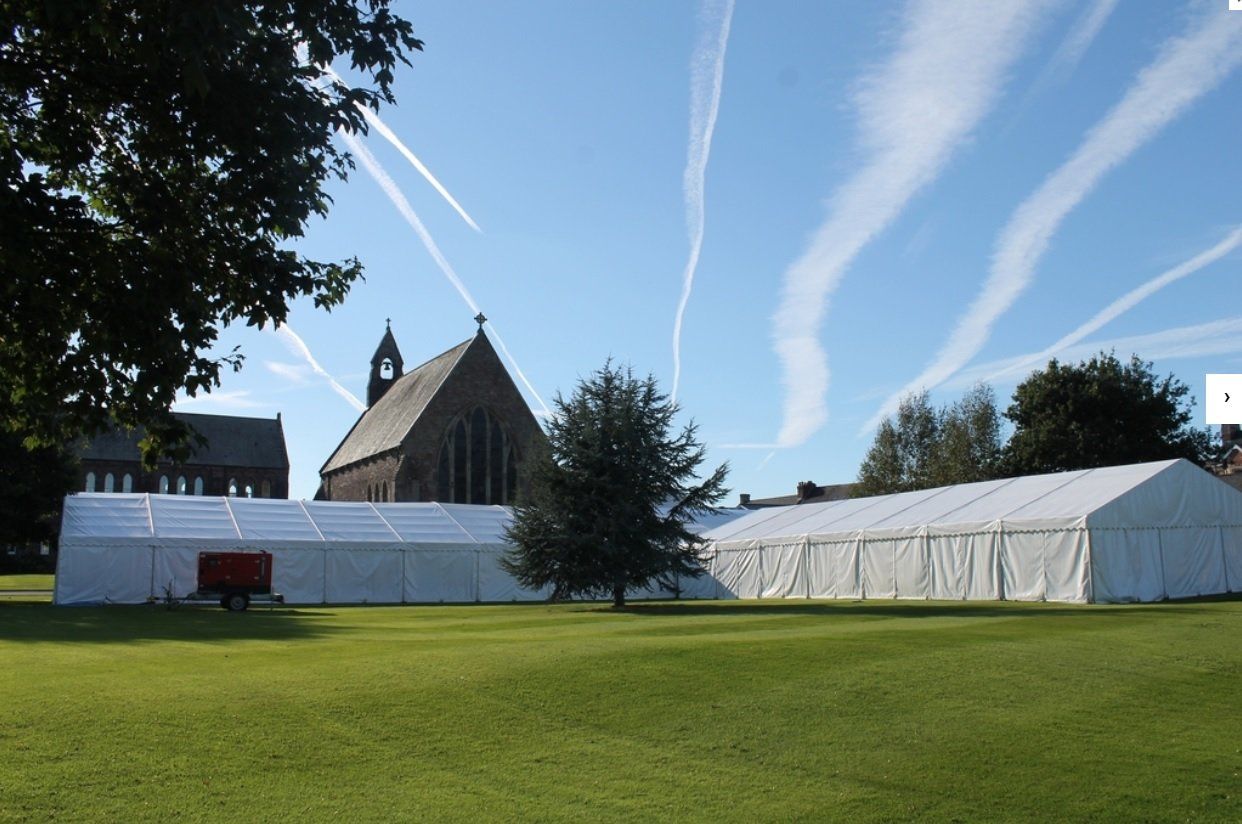 A large white marquee tent sits in a grassy field in front of a church