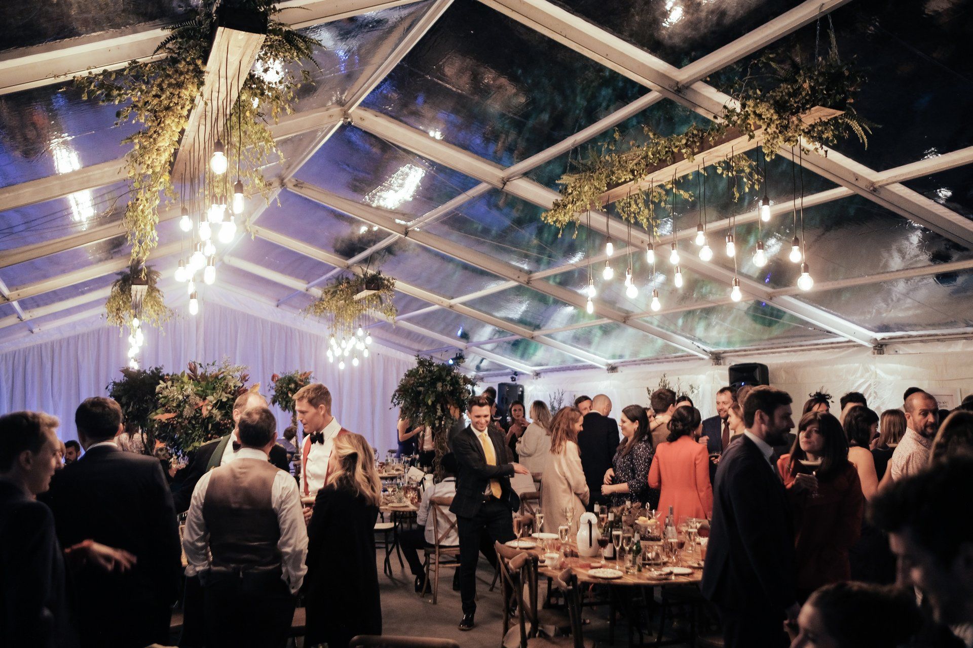 A large group of people are gathered under a clear roof at a party.