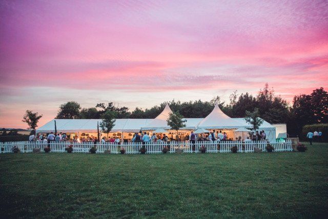 A large white tent is sitting in the middle of a field at sunset.