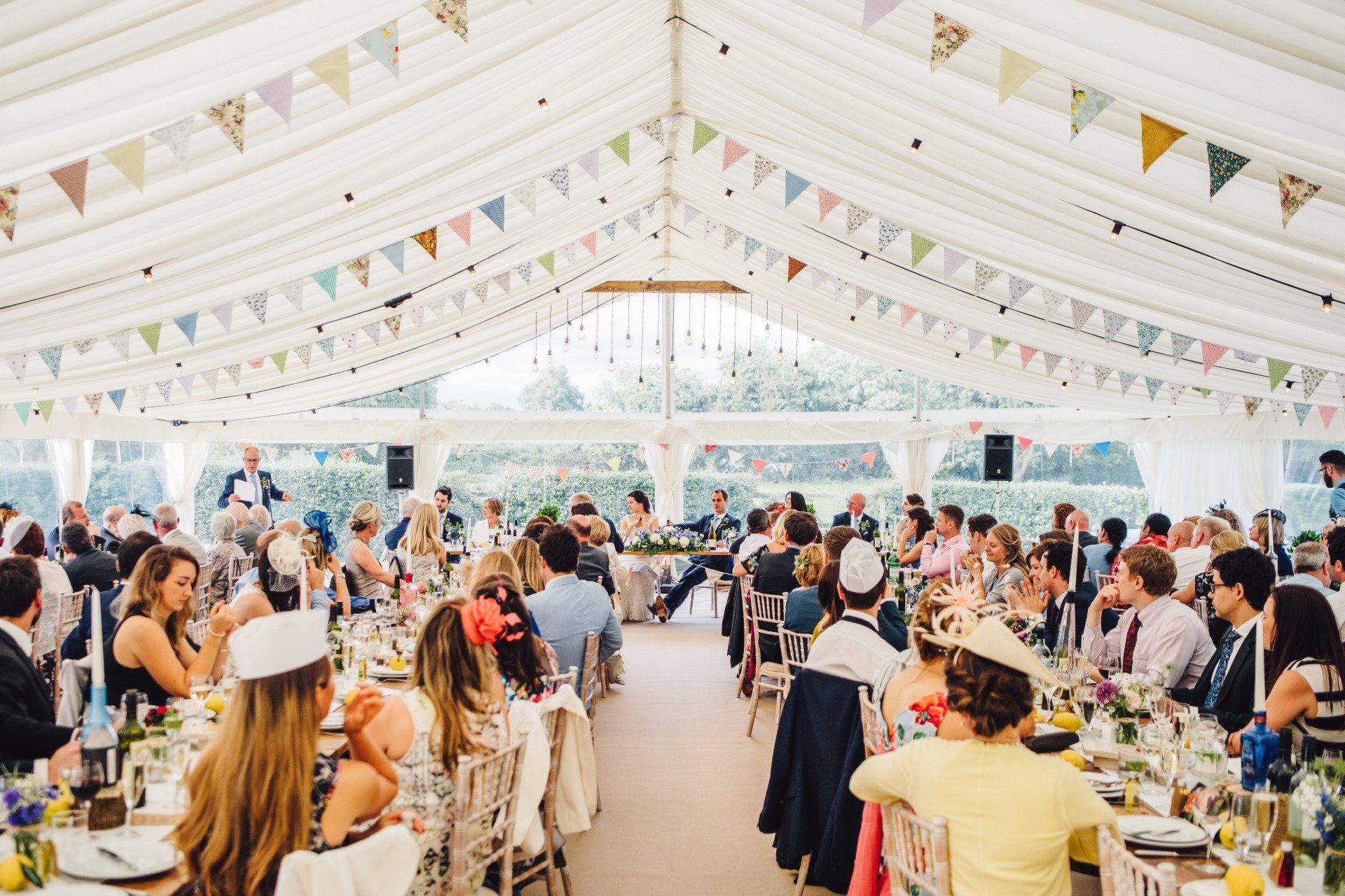 A large group of people are sitting at tables under a tent at a wedding reception.