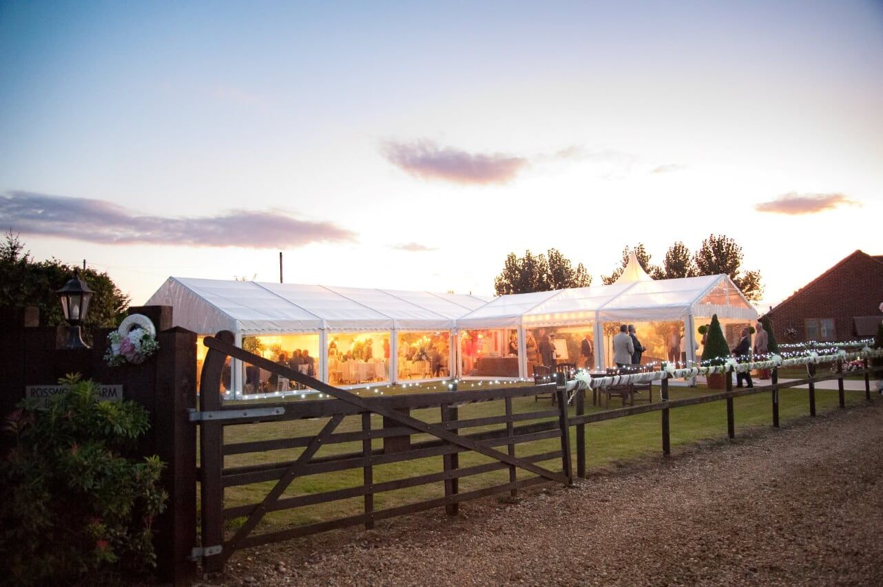 A large white tent is sitting in the middle of a field next to a wooden fence.