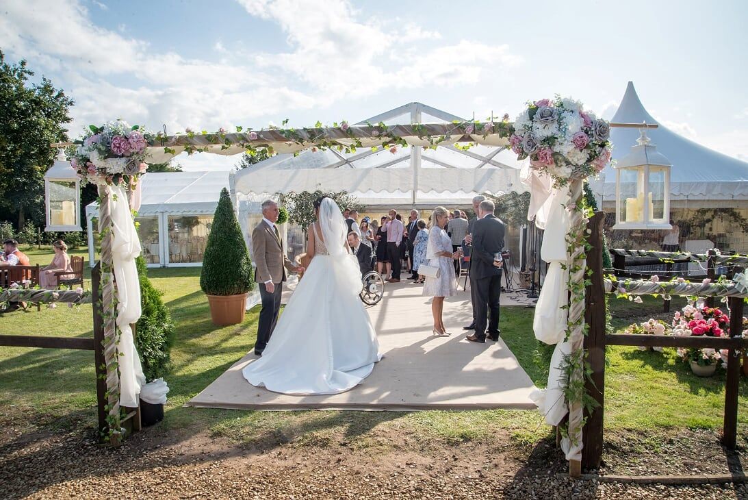 A bride and groom are standing under an archway in front of a tent.