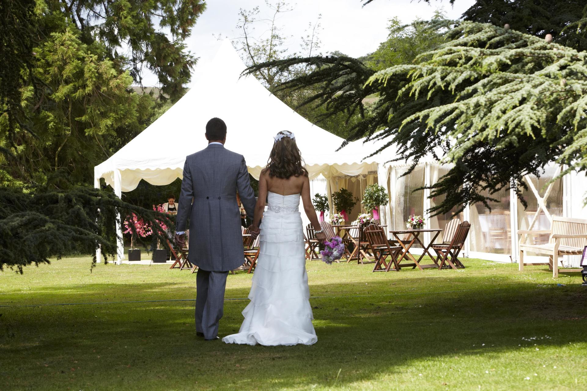 A bride and groom walking in front of a white tent