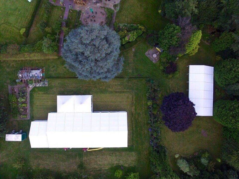 An aerial view of a large white marquee in a field surrounded by trees.