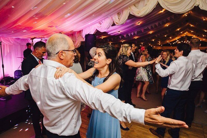 A group of people are dancing together at a wedding reception in a marquee