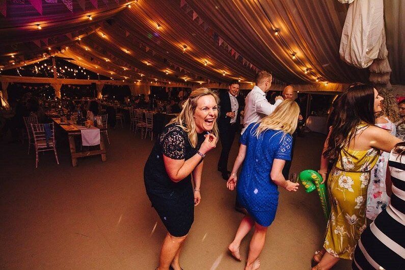 A group of people are dancing in a large marquee at a wedding reception.