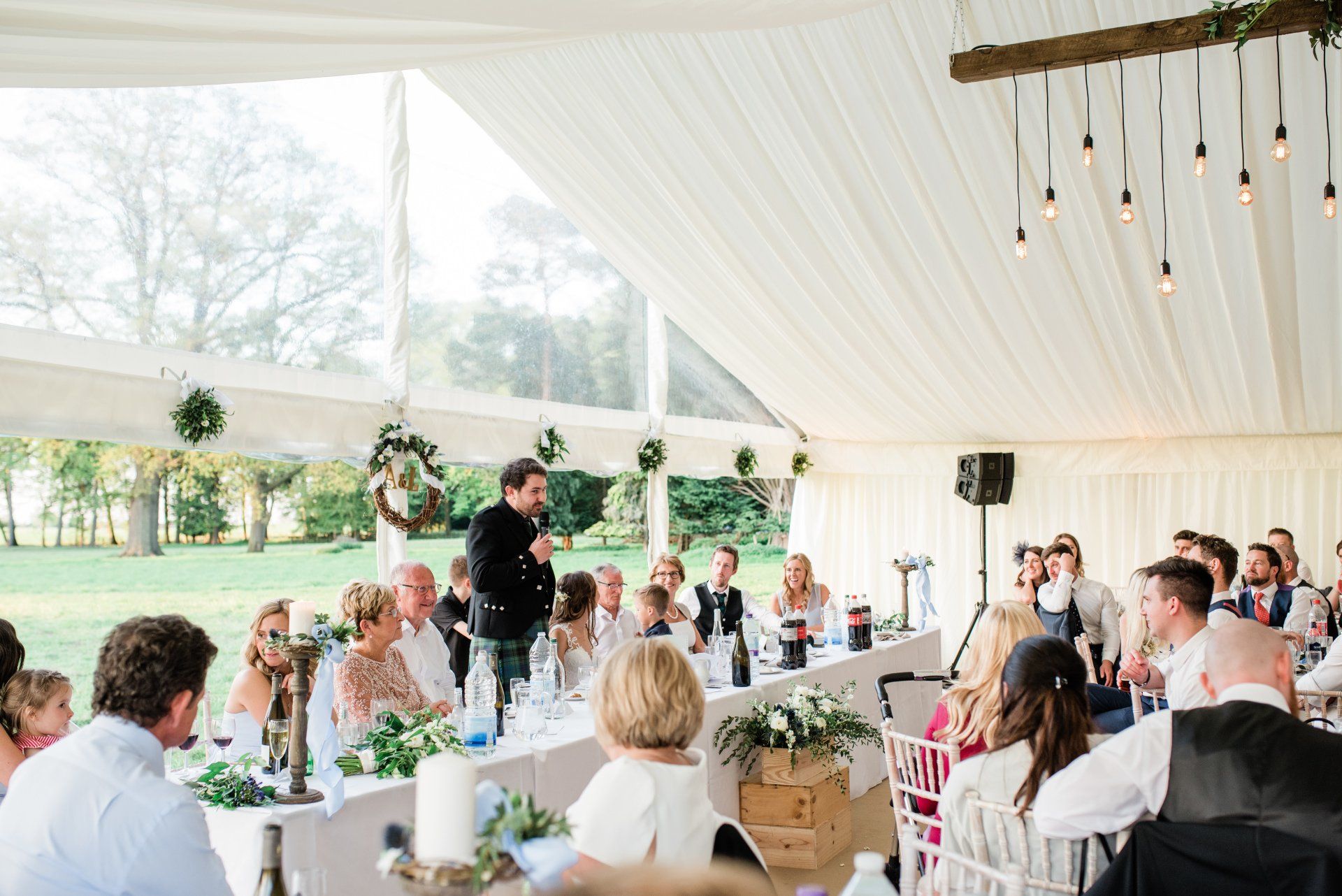 A man is giving a speech at a wedding reception in a tent.