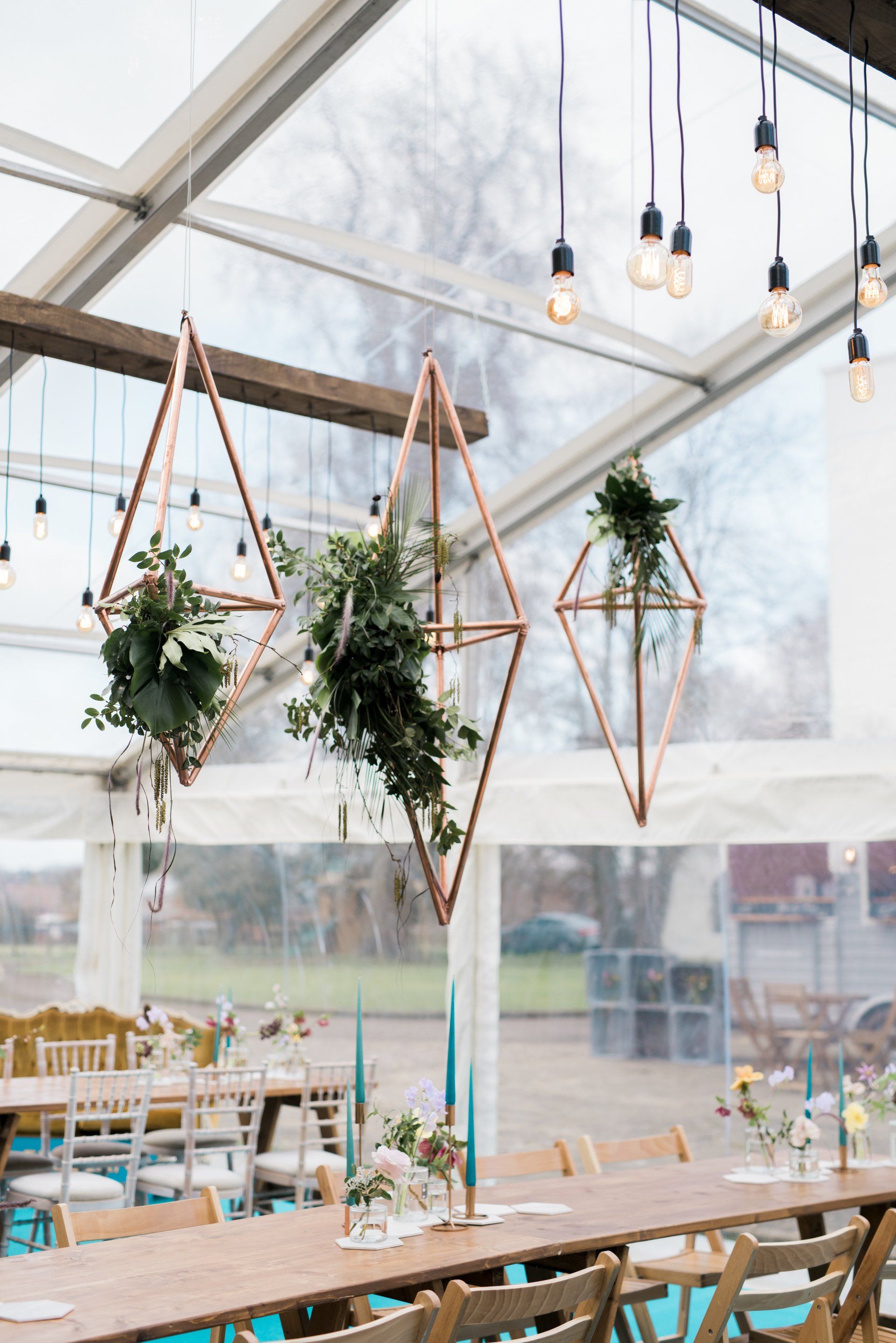 A long table with flowers hanging from the ceiling in a clear tent.