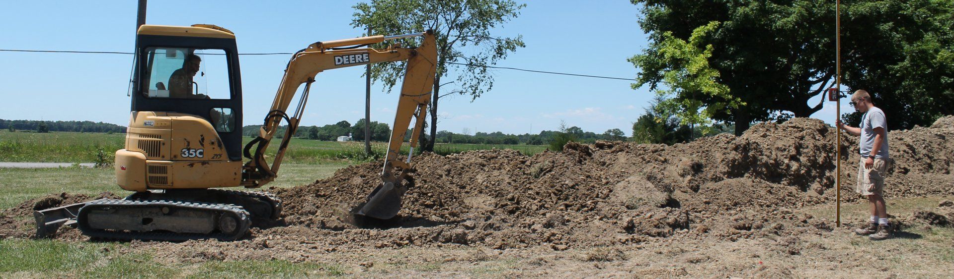 Excavator on a dirt lot beside a person under a blue sky.