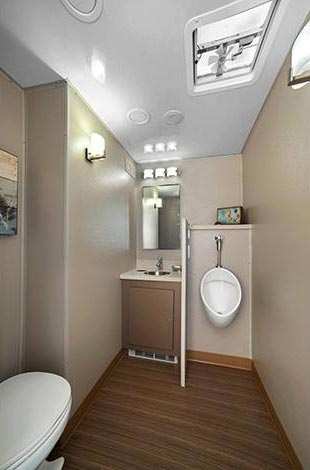 Narrow RV bathroom with toilet, sink, mirror, skylight, and wood-look floor.