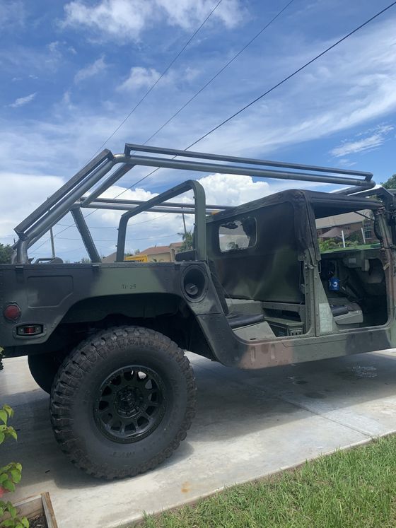 Camouflage Humvee with black roll cage frame on a driveway, blue sky background.