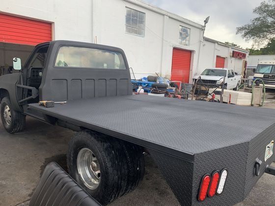 Black flatbed truck parked near a white building with red doors.
