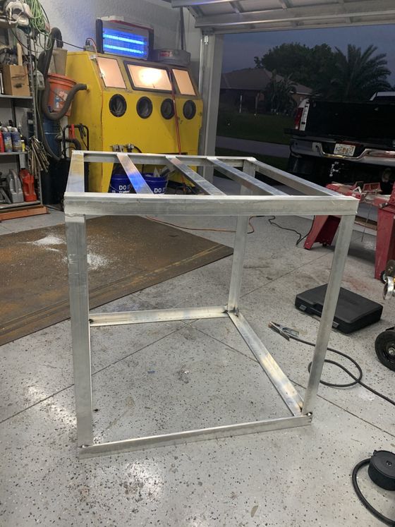 A welded aluminum frame, likely for a workbench, sits in a garage.
