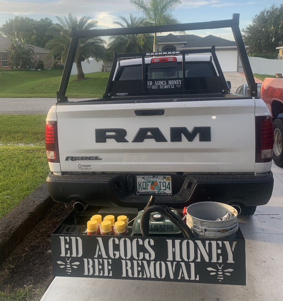 White RAM truck with ladder rack, honey bee removal sign, and bee removal equipment.