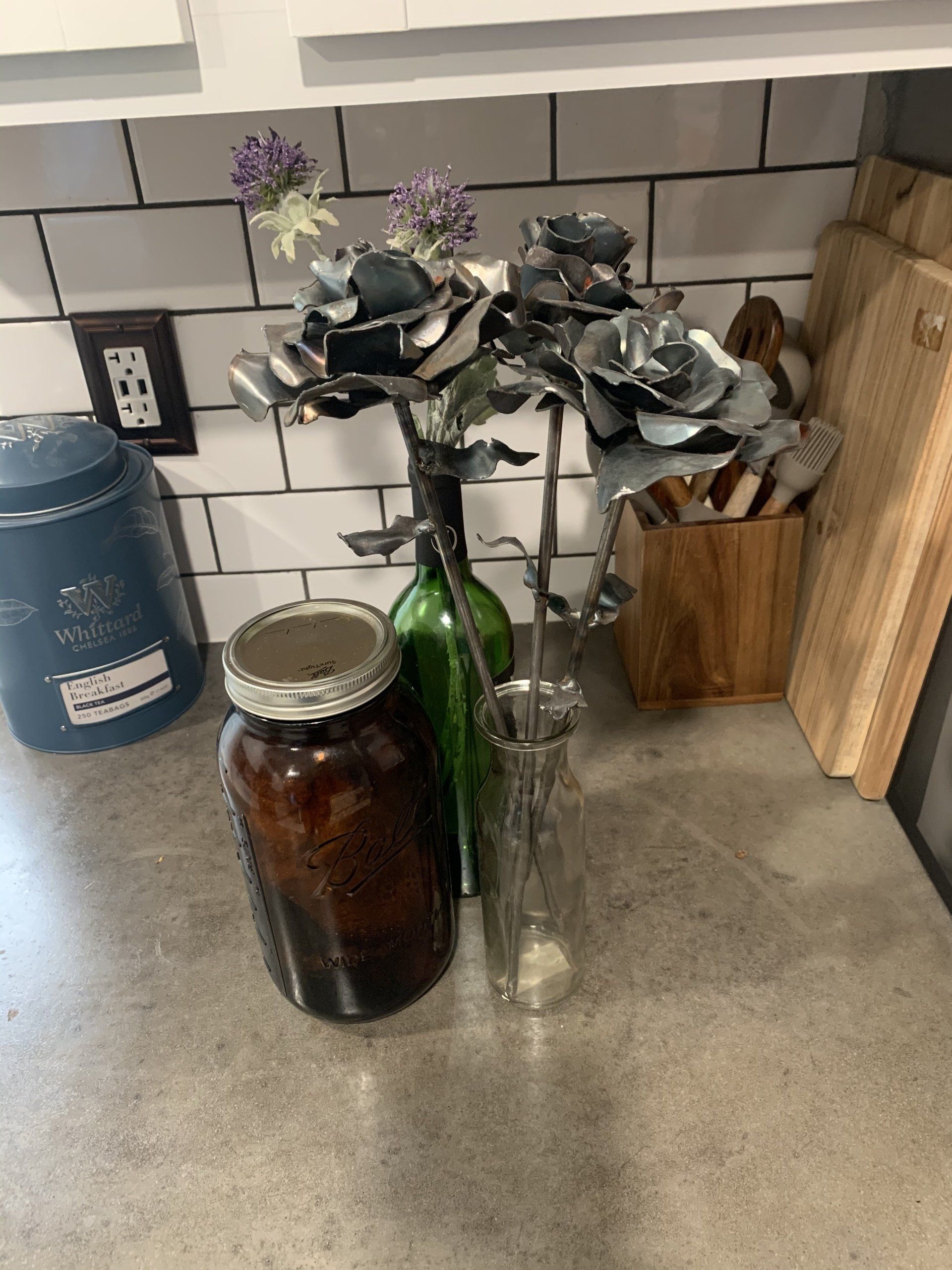 Mason jar and vases holding metal roses on a kitchen counter.