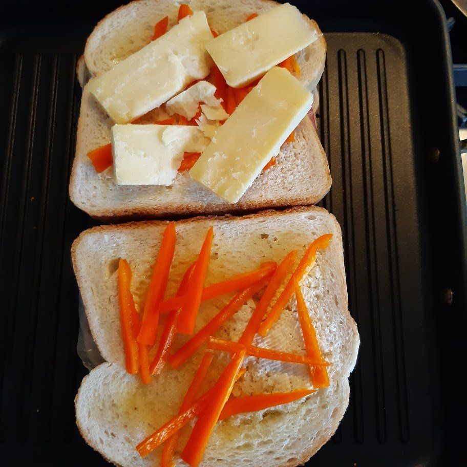 Ingrediënten voor een gegrilde sandwich: brood, wortelstaafjes en plakjes kaas op een bakplaat.