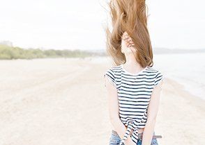 Vrouw op het strand die haar lange haar opgooit, gekleed in een gestreept shirt, op een zonnige dag.