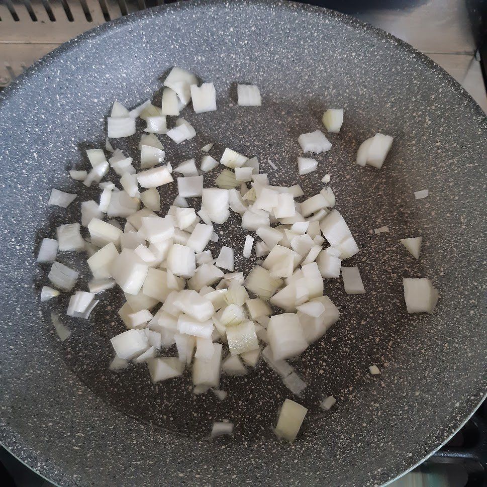 In een grijze koekenpan liggen gesneden uien klaar om te bakken.