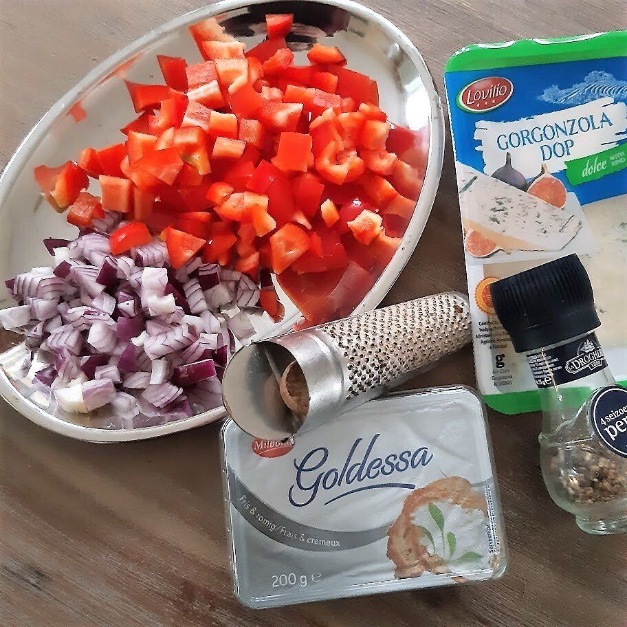 Gesneden rode paprika en rode ui in een schaal, Gorgonzola en Goldessa kaas, specerijen.