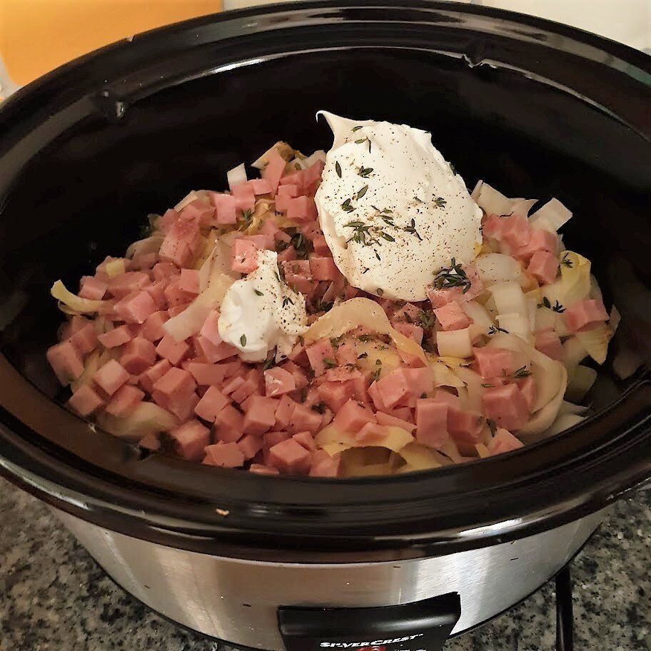 Slowcooker gevuld met blokjes ham, uien en zure room.