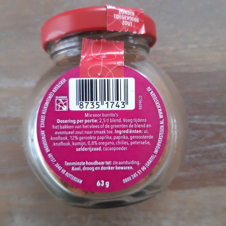 Klein glazen kruidenpotje met een rood deksel en etiket, gevuld met een kruidenmengsel, op een lichte ondergrond.